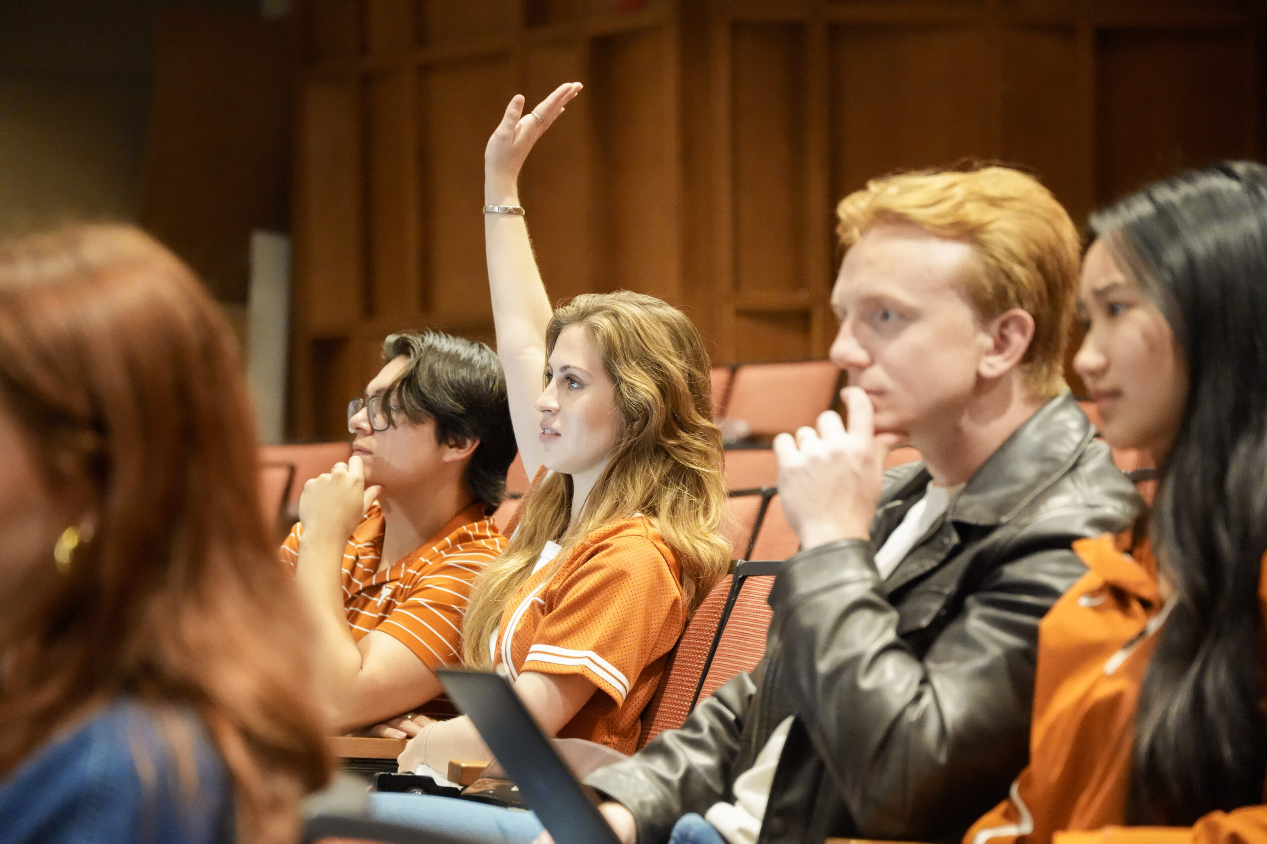 image of four students in a classroom, one is raising her hand