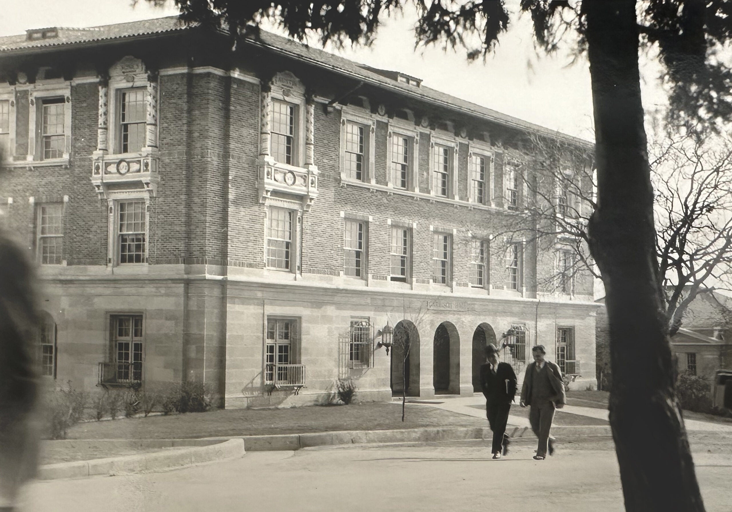 archival image of Garrison Hall on UT campus with two people walking in front