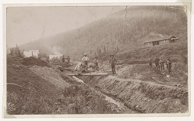 A black and white photo of gold miners in a creek.