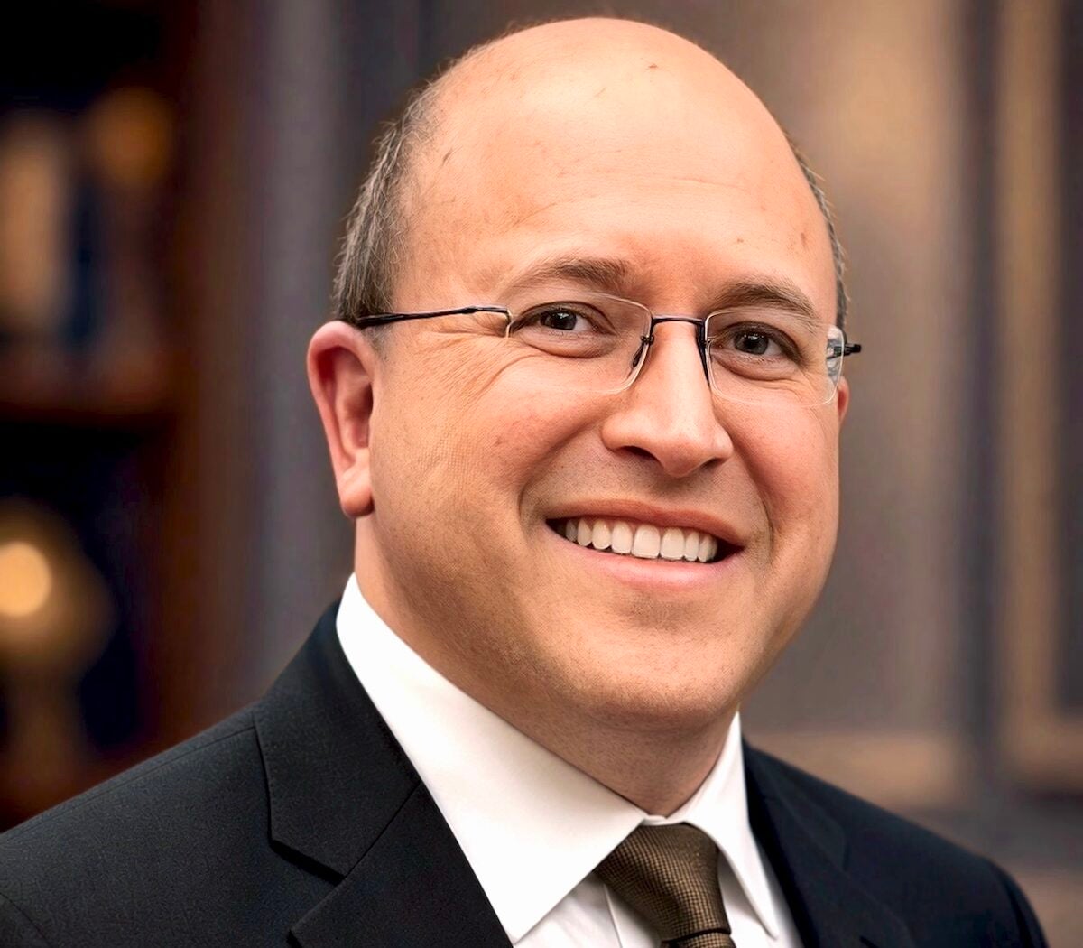 Man in suit, tie, and glasses poses outside in front of a building.