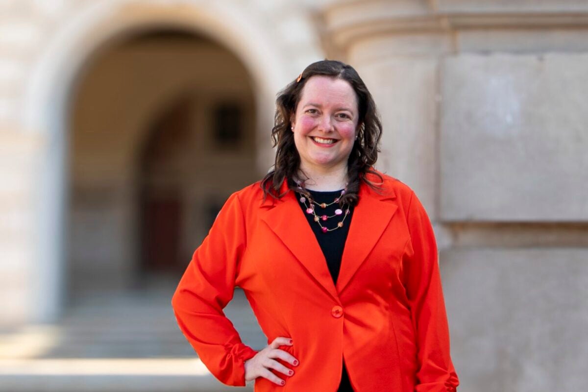 A woman in a red blazer poses for a photo, smiling with one hand on her hip