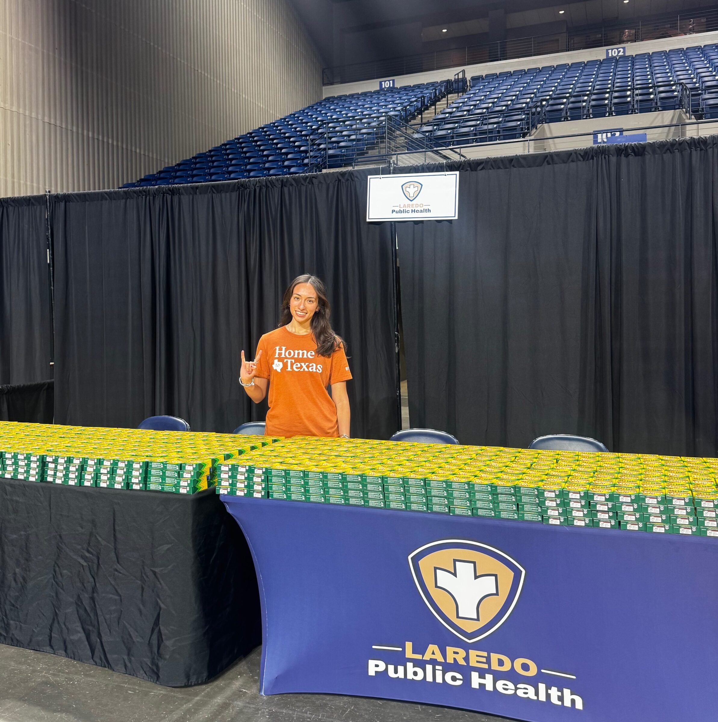 A girl wearing a burnt orange shirt stands in front of a table of small boxes.