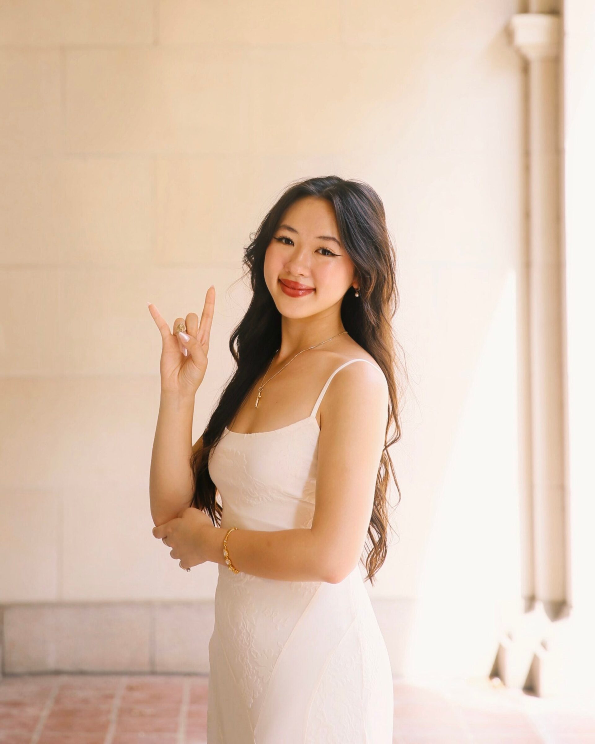 A woman wearing a white dress smiles for a photo while holding up the Hook 'Em, Horns hand sign.