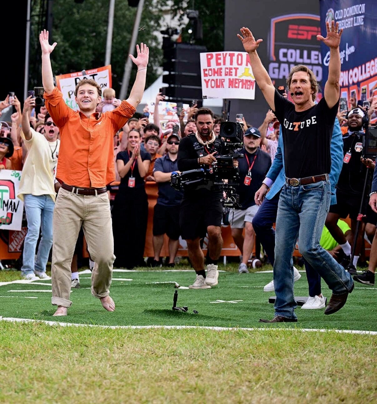 Two men jump with their arms raised above their heads while standing on a turf field.