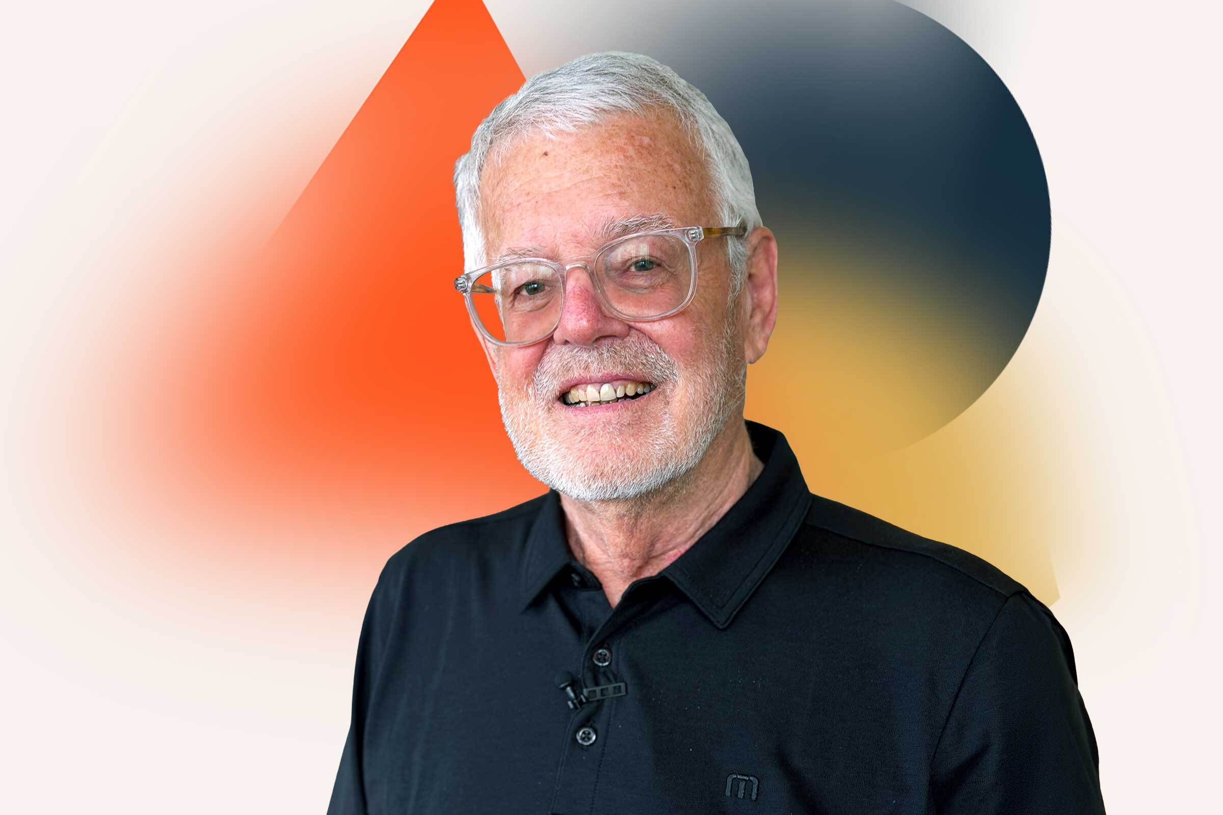 Allan MacDonald smiles in front of geometric background.