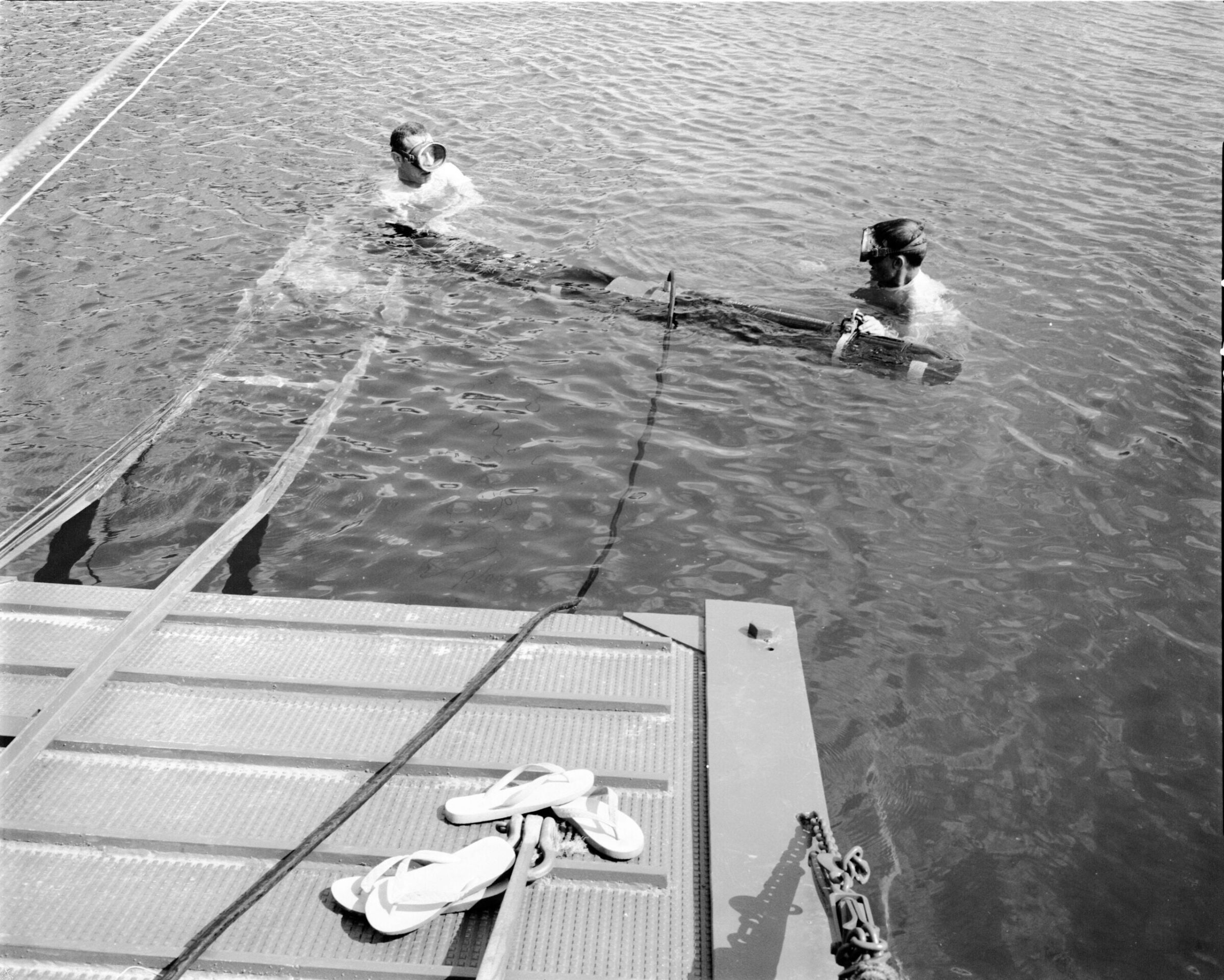 A black-and-white image of two people in the water with a diver-led sonar system.