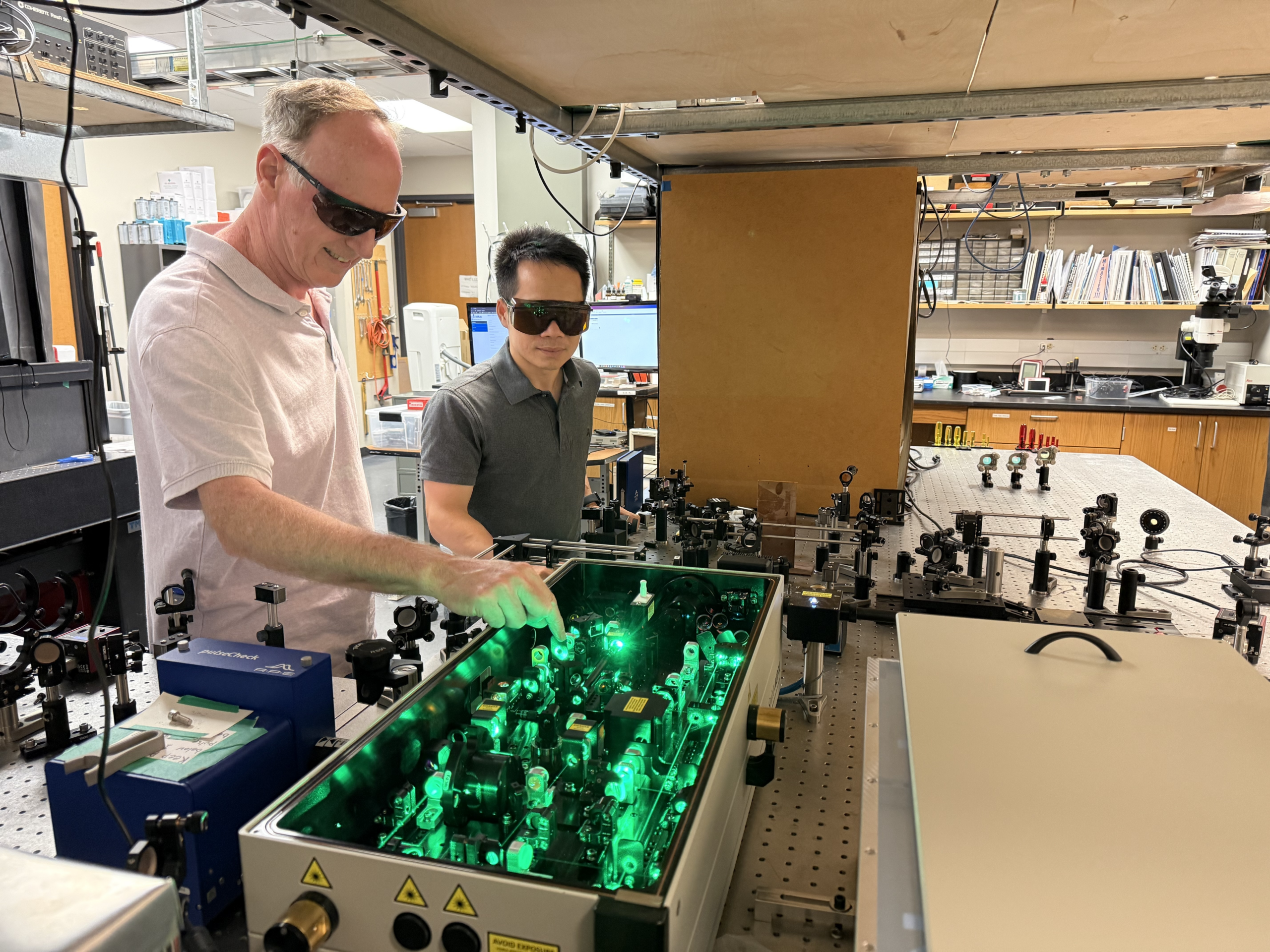 Two researchers work in a lab while wearing goggles.