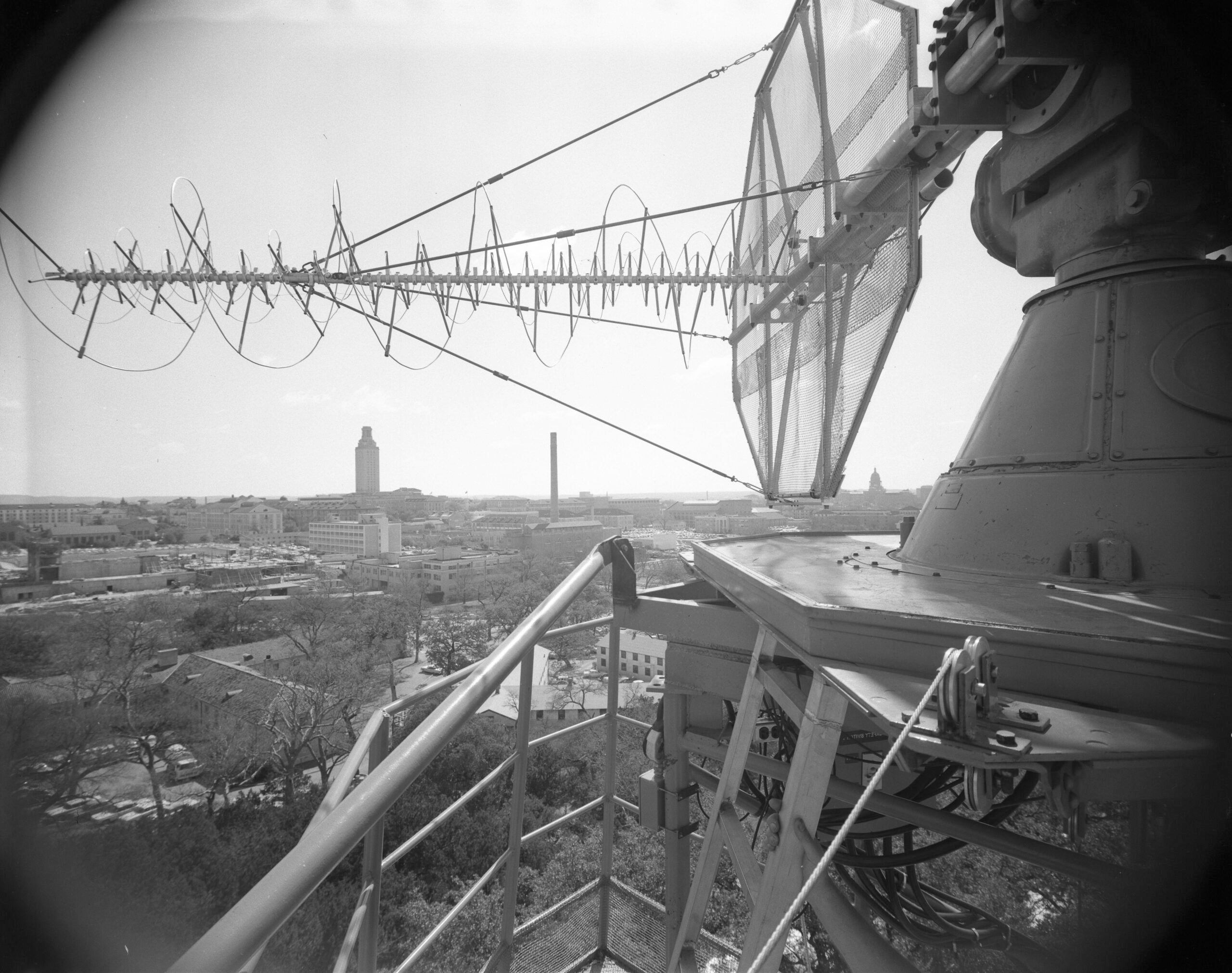 A black-and-white photo of a satellite with the University of Texas at Austin Tower in the background.