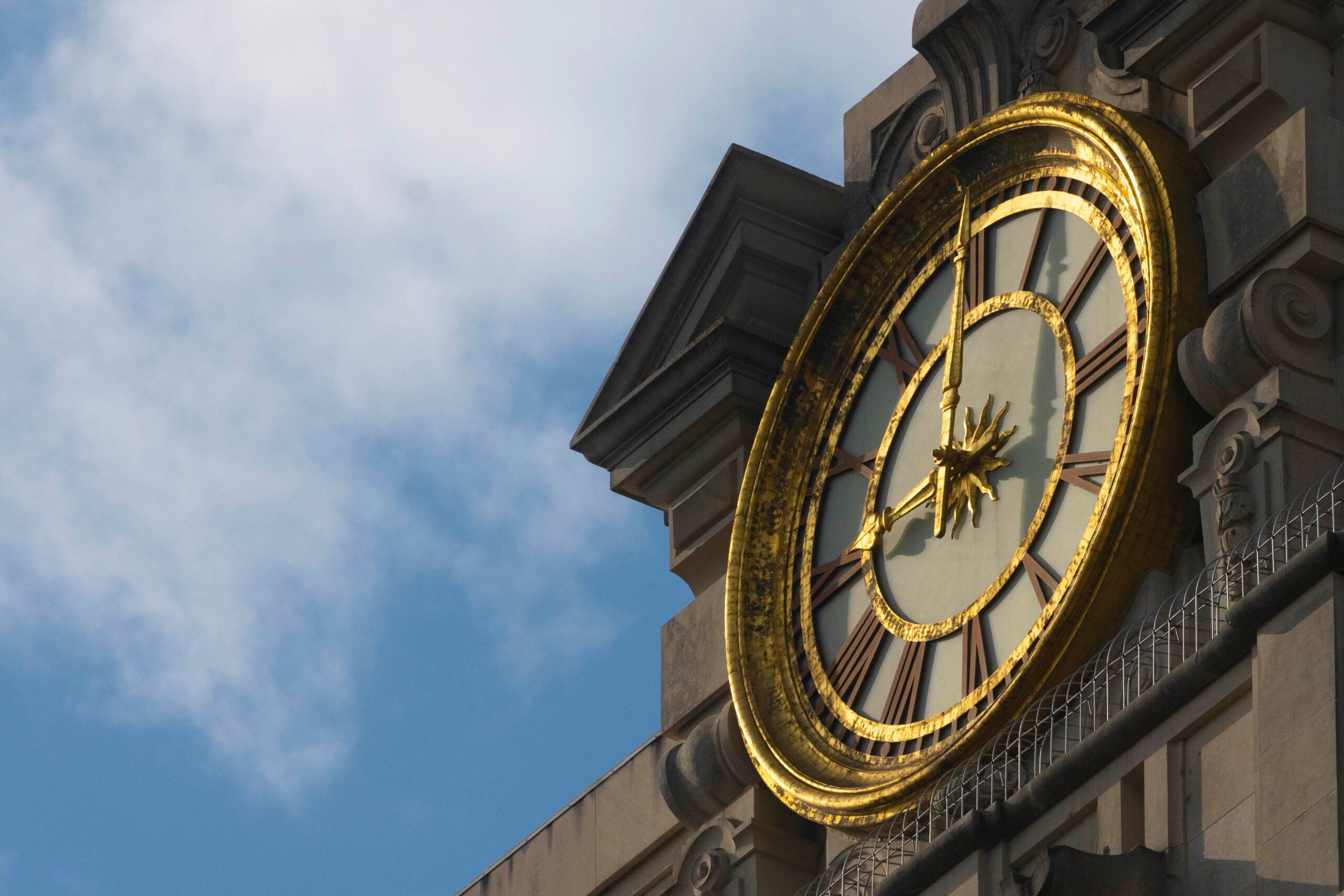 A close-up of the clock at the top of the University of Texas at Austin Tower with clouds in the background.