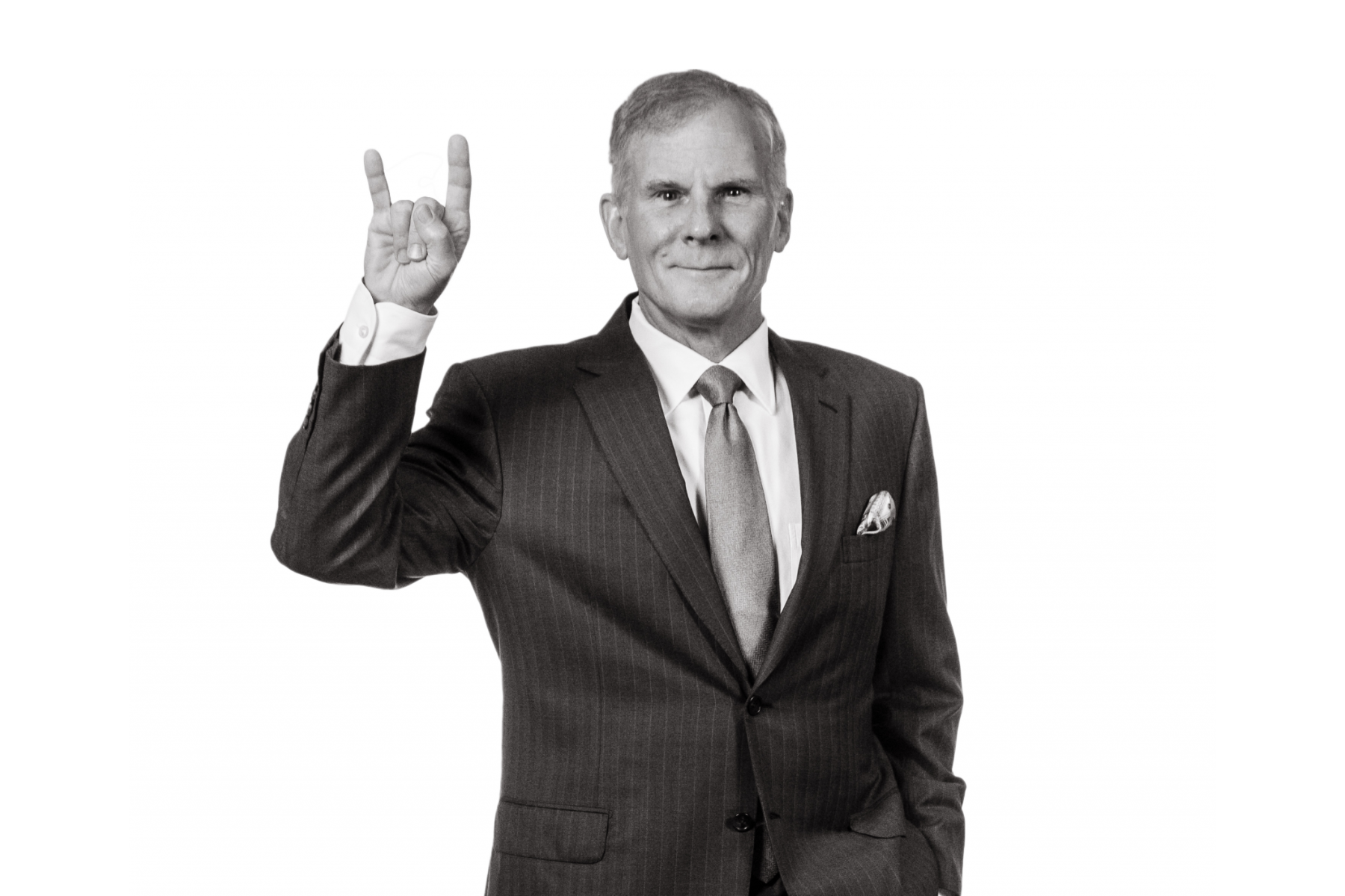 A black and white photo of a man in the a suit doing the Hook 'em Horns hand gesture