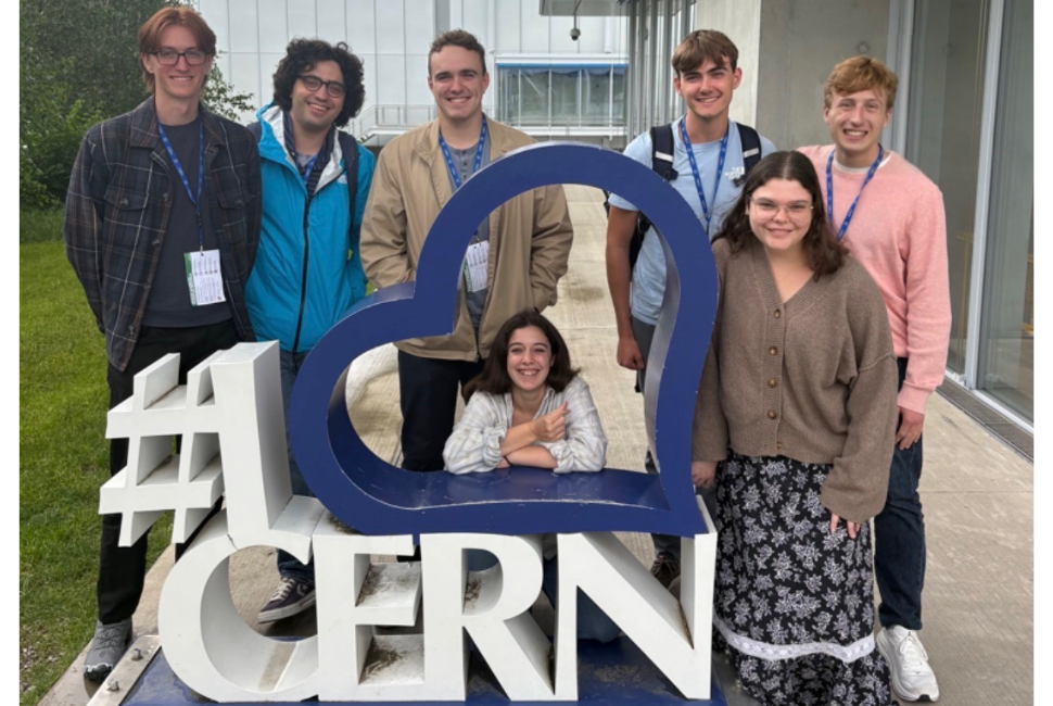 A group of students pose for a photo with a sculpture that says "I love CERN"