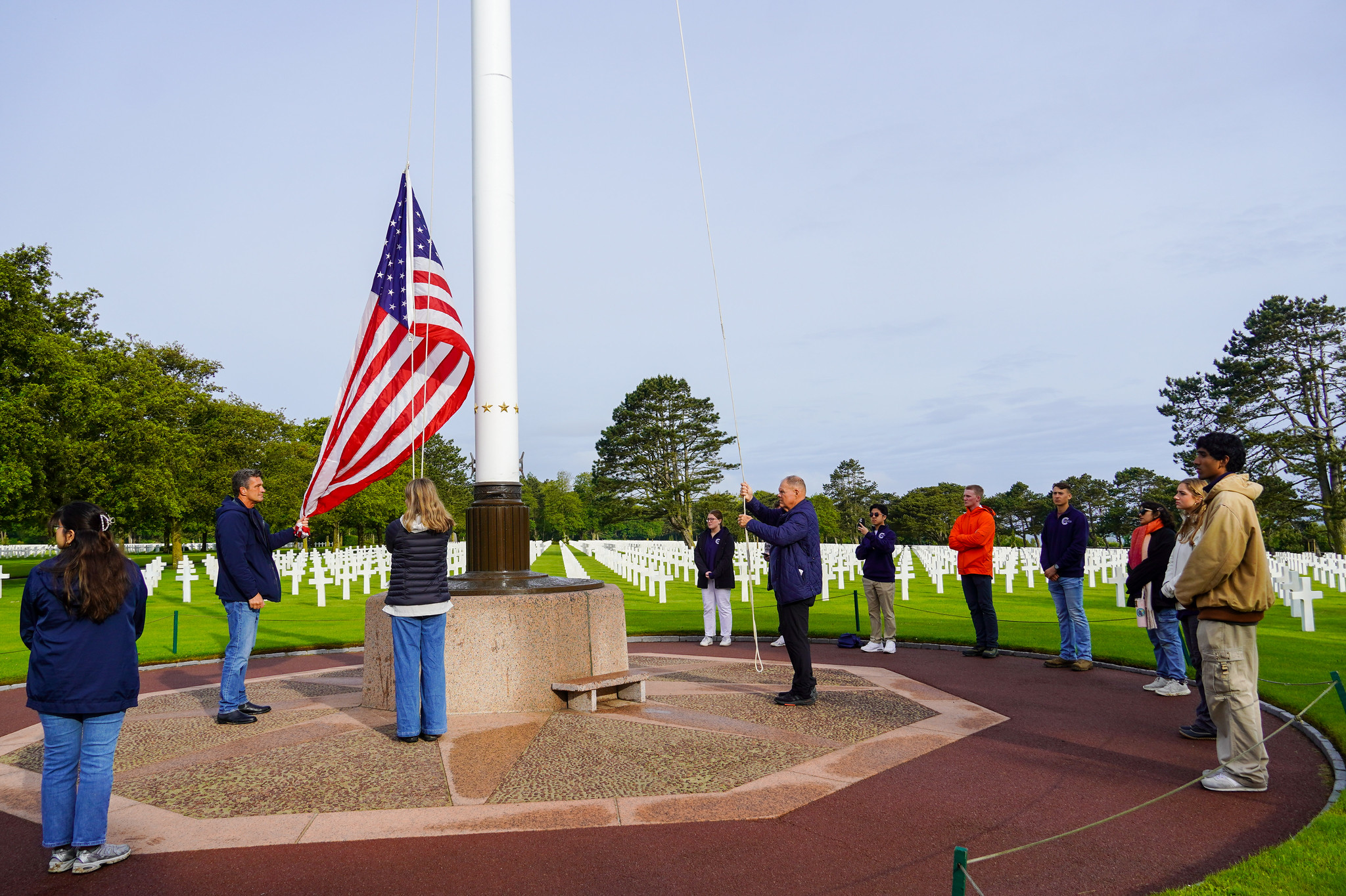 Undergraduate Longhorns raise the U.S. flag over the Normandy American Cemetery with former Commandant of the U.S. Marine Corps Gen. Robert Neller after visiting Omaha Beach at dawn during a trip led by the Clements Center.