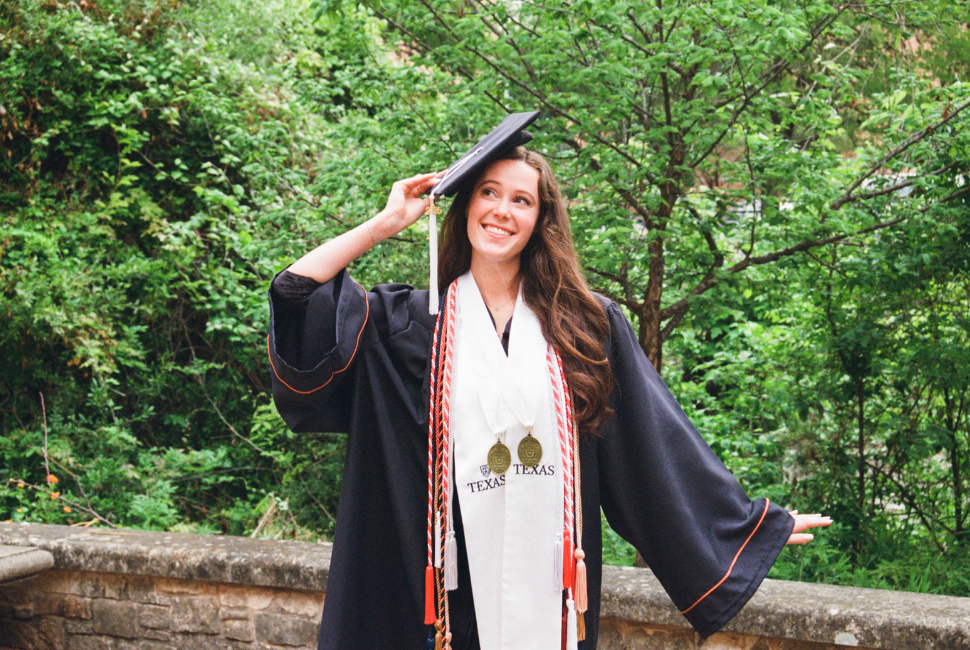 A student poses for a photo in a graduation cap and gown with cords and medals.