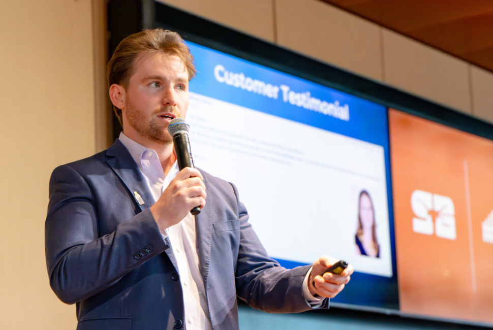 A man speaks into a microphone while giving and presentation.