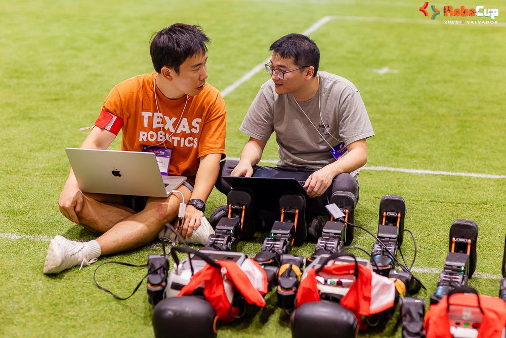 Two students prepare their child-sized humanoid robots for a match on a soccer field.