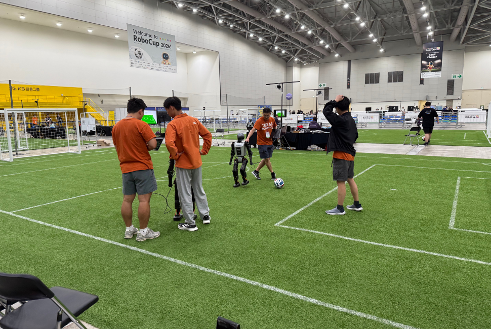 A research team works with humanoid robots on an indoor soccer field.