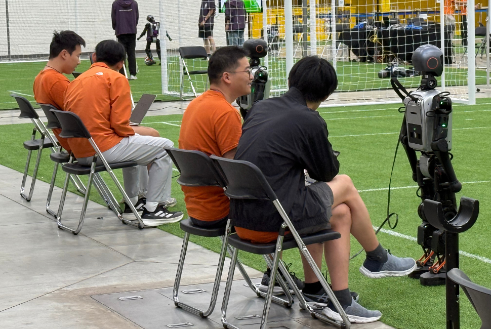 A research team works with humanoid robots on an indoor soccer field.
